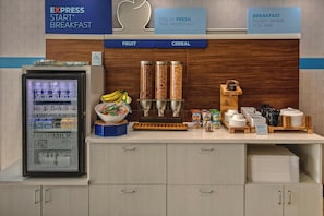 A breakfast station with a refrigerated display, fruit bowl, cereal dispensers, and a variety of food containers. - Holiday Inn Express Hotel & Suites Cookeville by IHG (Cookeville)
