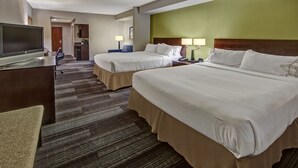 Ein Hotelzimmer mit zwei Betten, einem Schreibtisch mit Fernseher, einer kleinen Küchenzeile und einem im Hintergrund sichtbaren Badezimmer.
