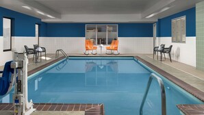 An indoor swimming pool with a clear blue water, surrounded by white and blue walls, and furnished with orange and black chairs. - Hampton Inn Knoxville East (Knoxville)