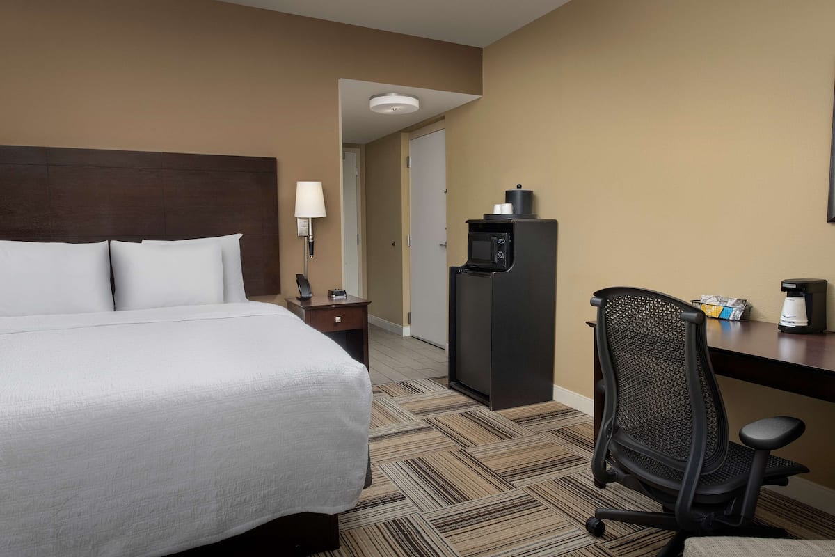 A hotel room with a bed, a desk with a chair, a microwave, and a lamp.