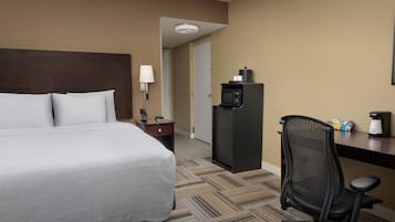 Quarto de hotel com uma cama, uma escrivaninha com cadeira, um micro-ondas e um abajur.