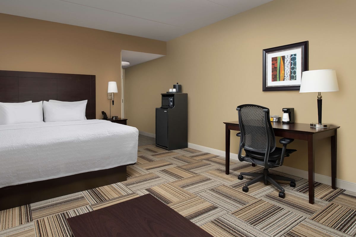 A hotel room with a bed, desk, chair, and a refrigerator.