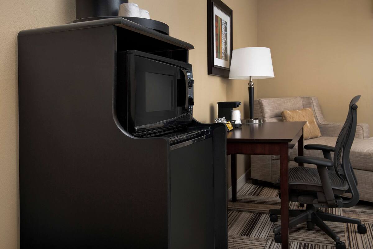 A compact kitchenette with a microwave, a small refrigerator, a coffee maker, and a table with a chair.