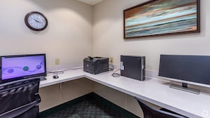 Ein Computertisch mit einem Desktop-Computer, einem Drucker und einem Bildschirm. An der Wand hängt eine Uhr und über dem Tisch hängt ein Gemälde.