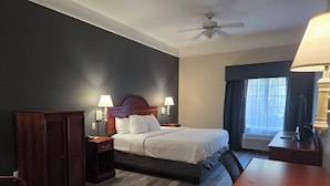 Ein Hotelzimmer mit Bett, Nachttischen, Schreibtisch, Stuhl, Kleiderschrank und Deckenventilator.