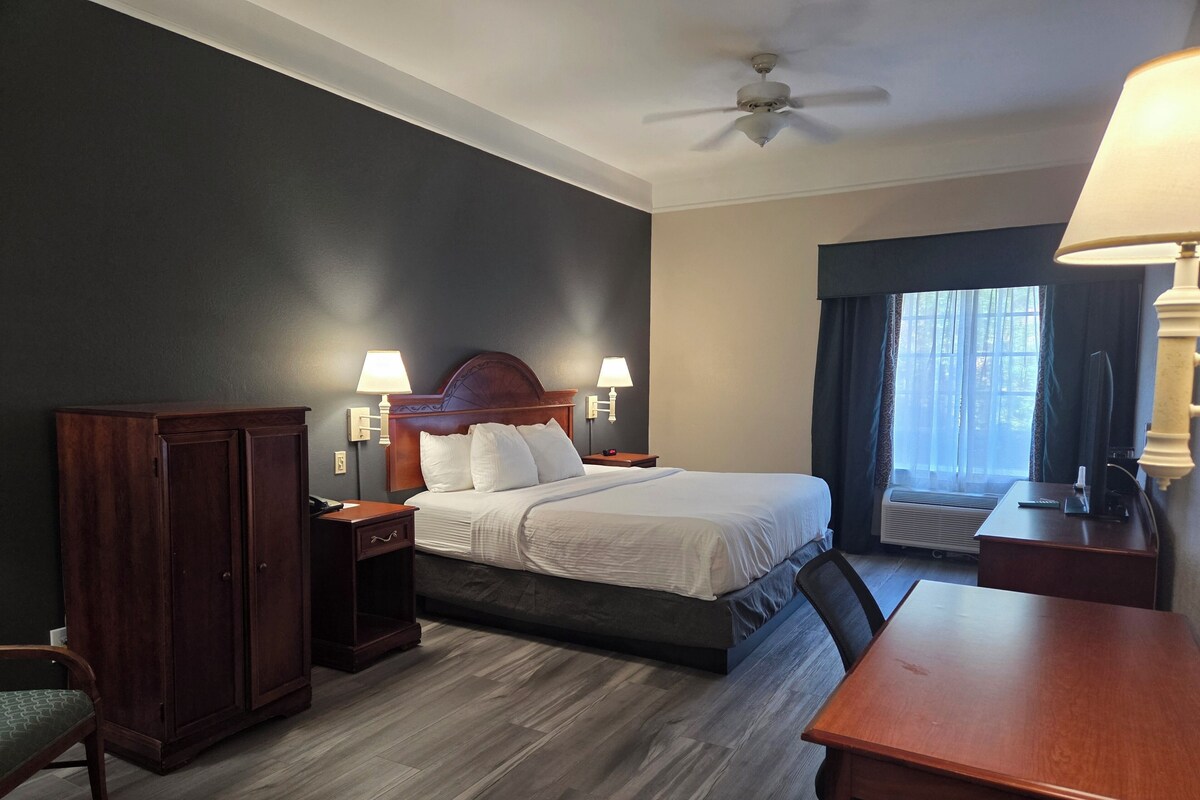 A hotel room with a bed, bedside tables, a desk, a chair, a wardrobe, and a ceiling fan.