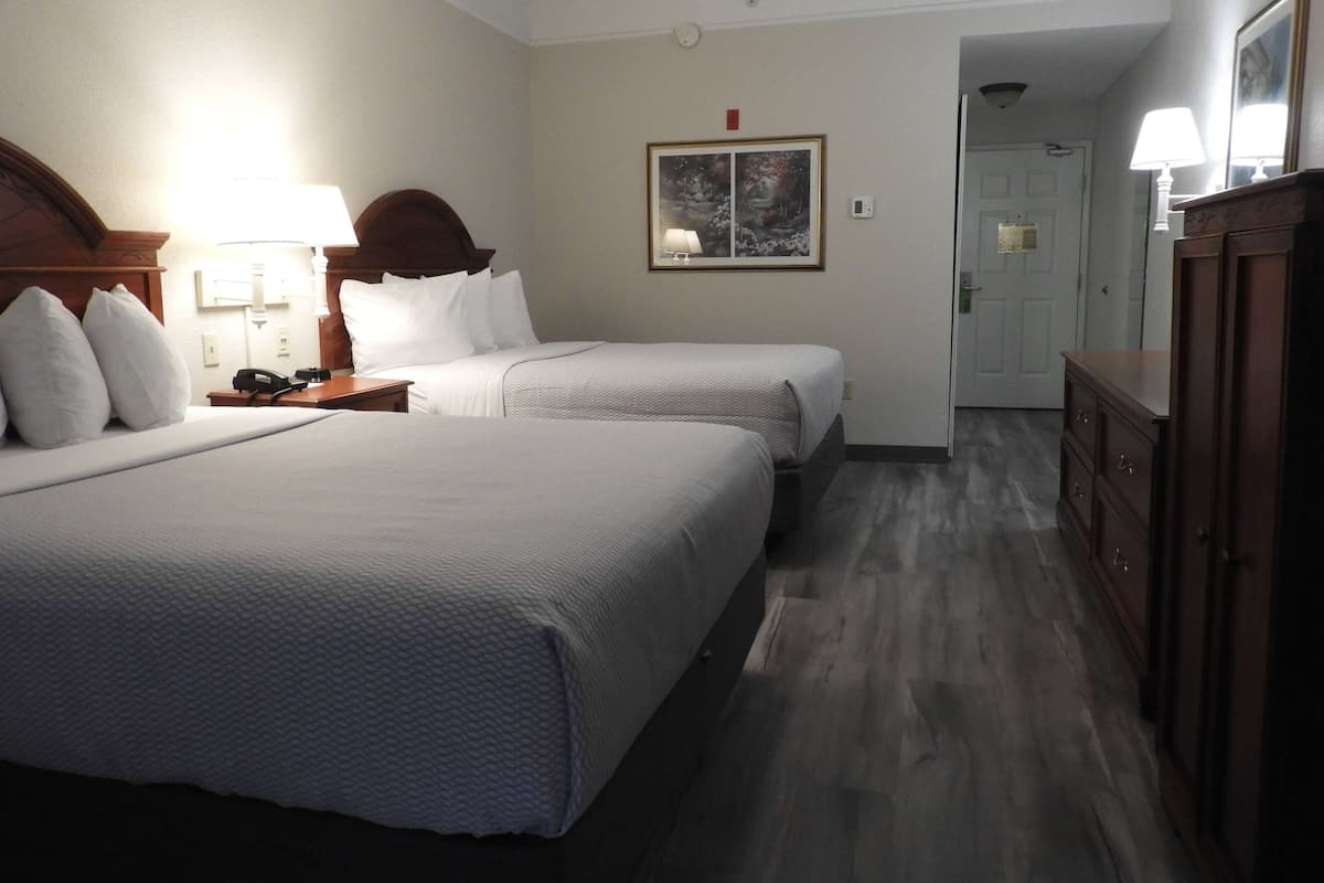 Une chambre d’hôtel avec deux lits, une table de chevet avec une lampe, un tableau au mur et une commode en bois.