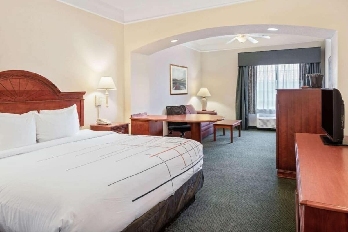 Une chambre d’hôtel avec un grand lit, un bureau, une chaise, une télévision et une fenêtre avec des rideaux.