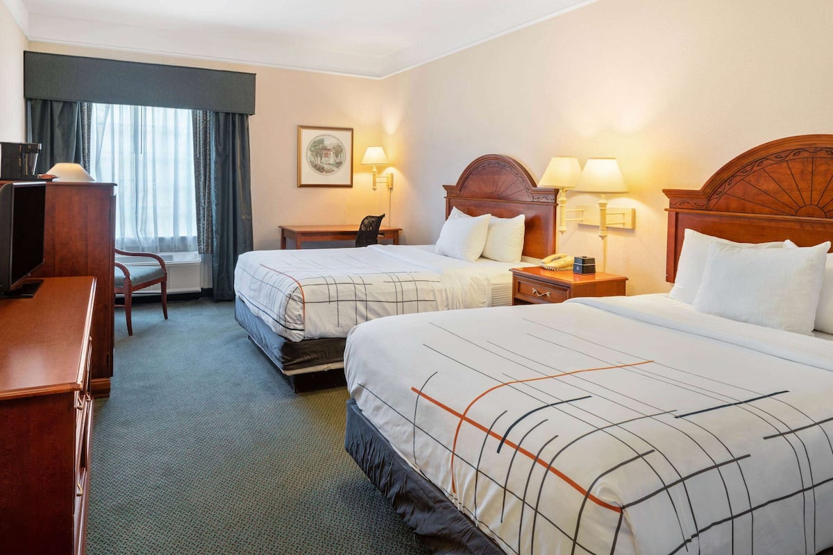 Une chambre d’hôtel avec deux lits, un bureau, une chaise, une lampe et un tableau au mur.