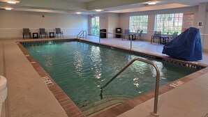 An indoor swimming pool with clear water, surrounded by lounge chairs and a covered seating area. - Stay Well Inn & Suites (Fort Myers)