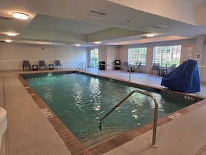 An indoor swimming pool with clear water, surrounded by lounge chairs and a covered seating area. - Stay Well Inn & Suites (Fort Myers)
