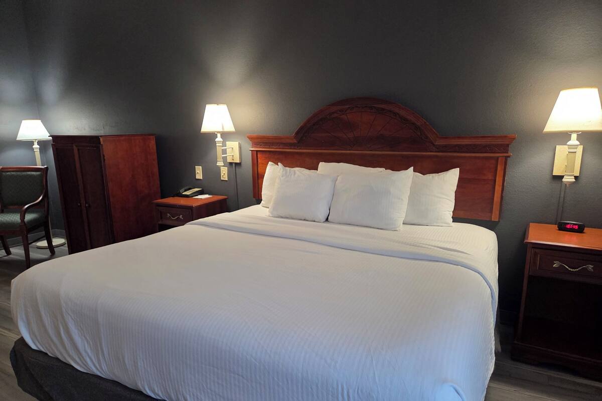 Une chambre d’hôtel avec un grand lit, deux tables de chevet, une tête de lit en bois et deux lampes fixées au mur.