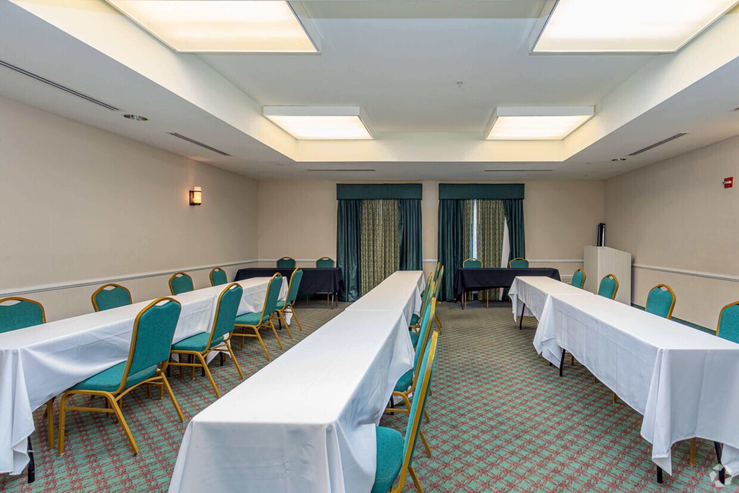 Une salle de conférence avec de longues tables et des chaises, un tapis à motifs et un plafond doté de lucarnes.