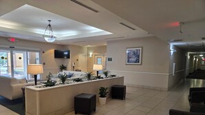A hotel lobby with a reception desk, seating area, and a hallway. - Stay Well Inn & Suites (Fort Myers)