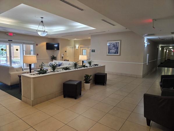 A hotel lobby with a reception desk, seating area, and a hallway. - Stay Well Inn & Suites (Fort Myers)