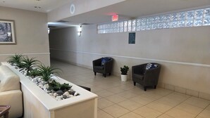 A reception area with a reception desk, two armchairs, a potted plant, and a wall-mounted sign. - Stay Well Inn & Suites (Fort Myers)