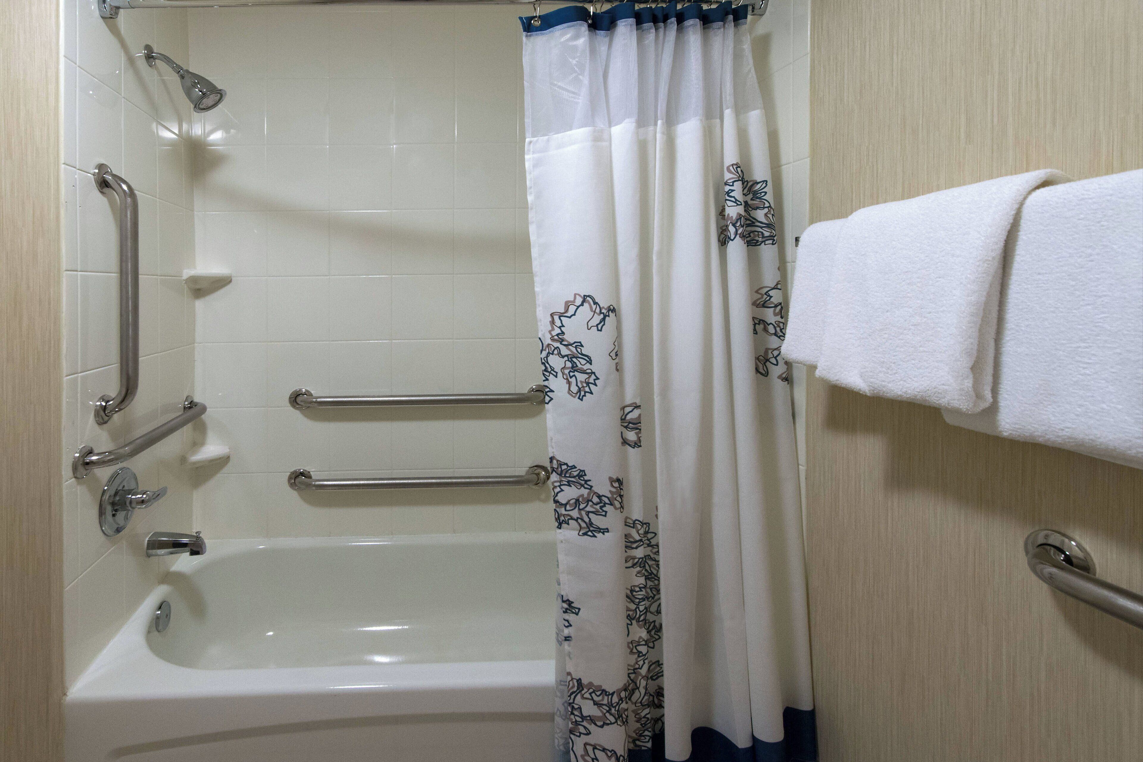 Un baño con bañera, barras de apoyo, cabezal de ducha y un perchero.