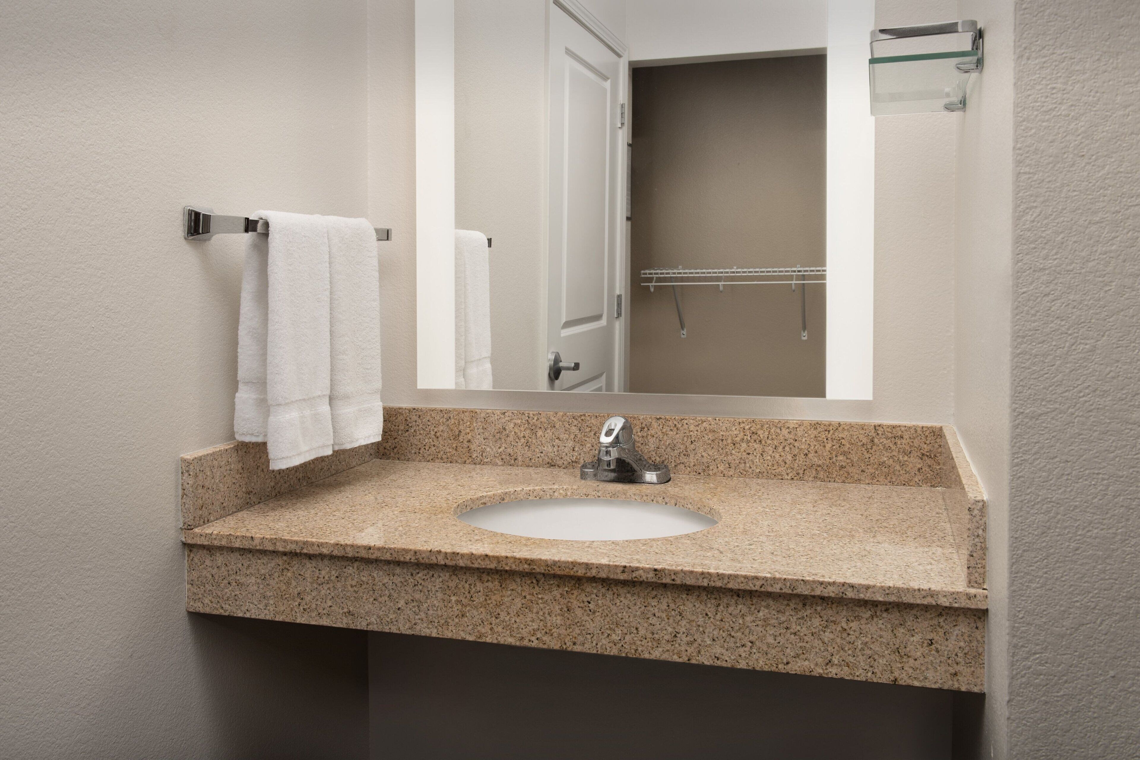 A bathroom with a granite countertop sink, a mirror, and a towel rack.