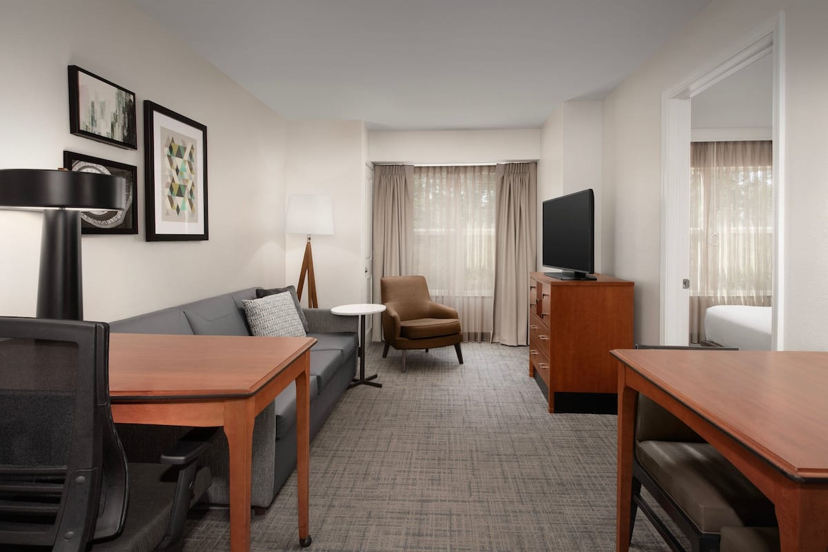 Habitación de hotel con sofá, sillón, televisión y una mesita.