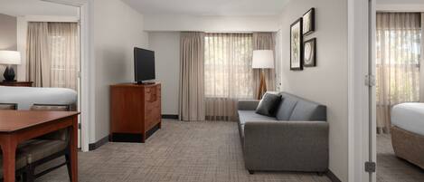Quarto de hotel com cama, sofá, televisão, secretária e cómoda.