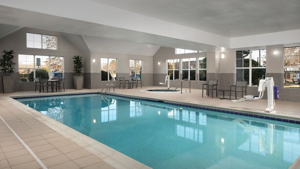 Una piscina interior con agua cristalina, rodeada de suelo de baldosas y algunas sillas.