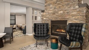 Un área de estar moderna con chimenea de piedra, sillones de cuero y un comedor al fondo.