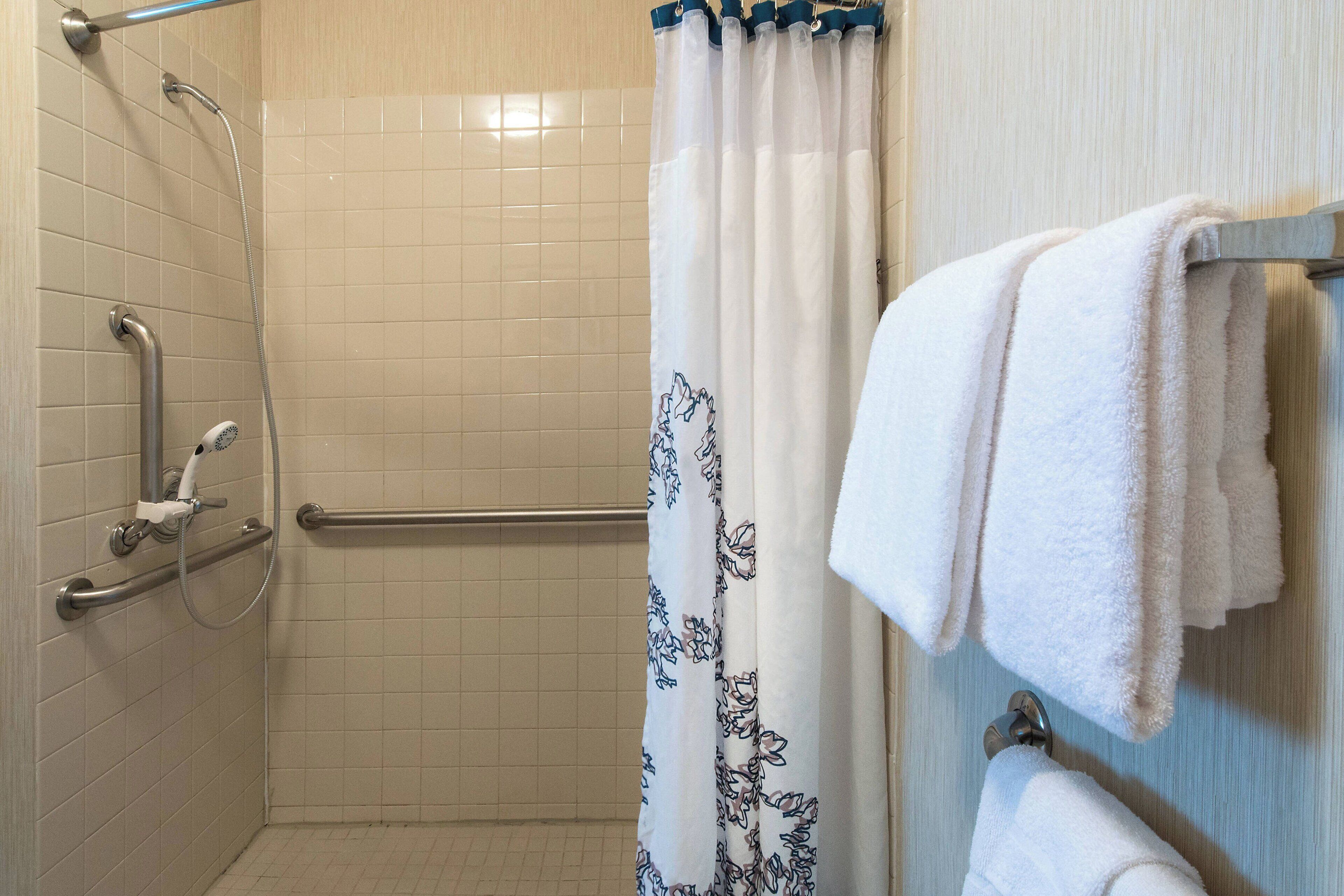 A shower area with a handrail, a showerhead, and a curtain with a floral pattern.