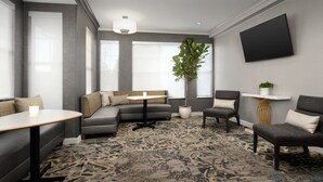 Una sala de estar moderna con un sofá gris, una mesa redonda, una planta en maceta y un televisor de pantalla plana montado en la pared.