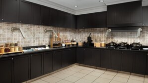 Una cocina moderna con armarios oscuros, salpicadero de azulejos y una isla central con distintos utensilios de cocina.