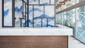 A reception desk with a marble top, a wall with abstract blue and white artwork, and a modern light fixture.