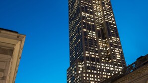 A tall, illuminated skyscraper with a spire, surrounded by other buildings.