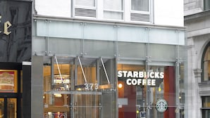 A Starbucks Coffee with a glass storefront, a visible entrance, and a potted plant in front.