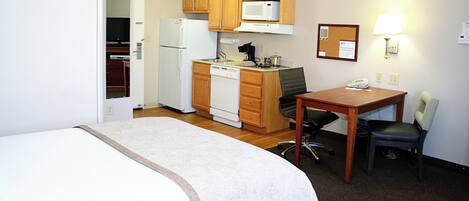 A hotel room with a bed, a desk, a chair, a microwave, a refrigerator, and a small kitchenette.