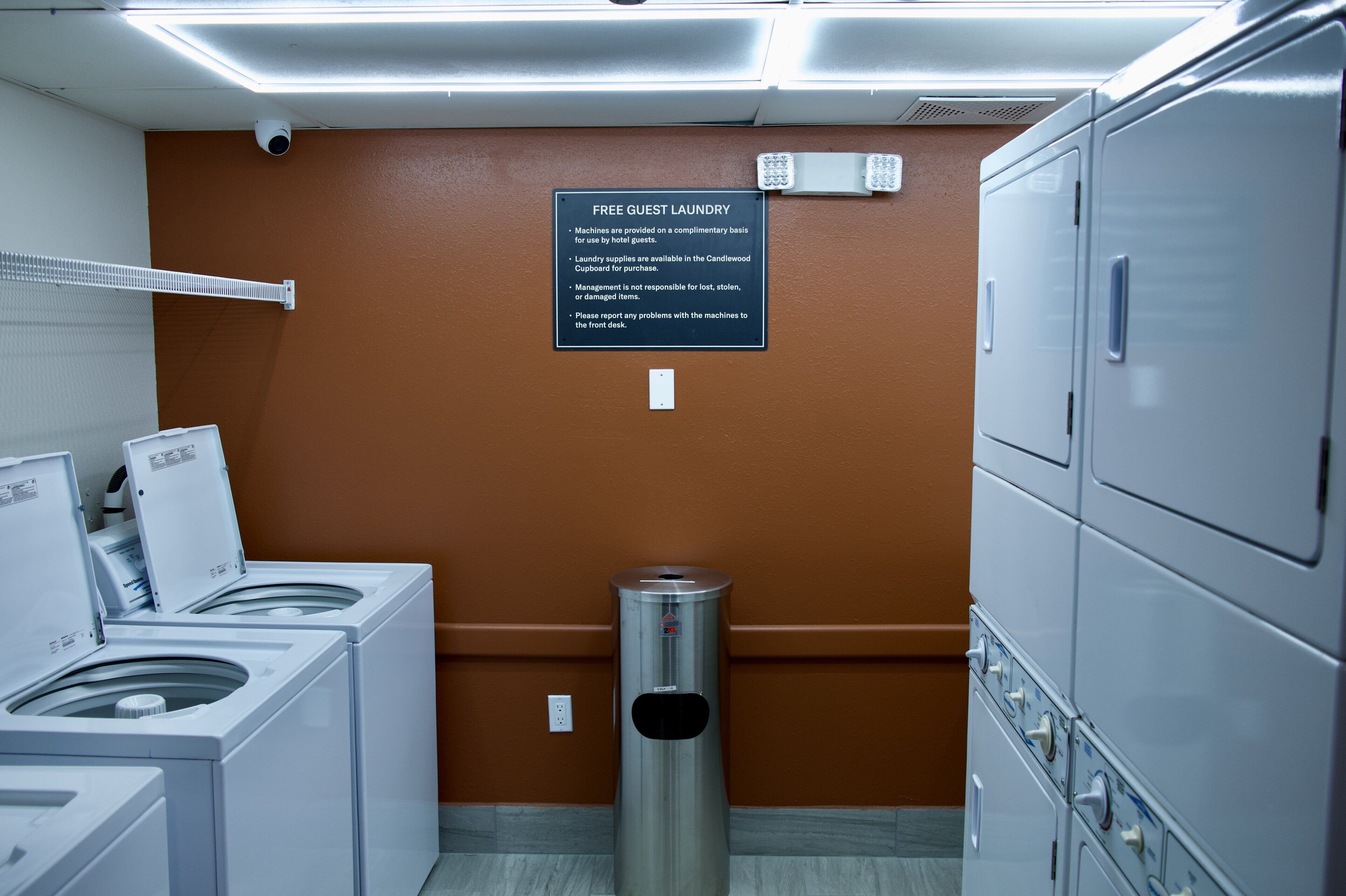A laundry area with washers and dryers, a sign about free guest laundry, and a trash can.