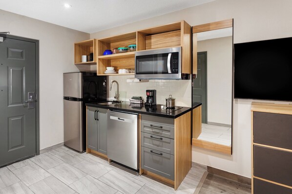 Una cocina moderna con electrodomésticos de acero inoxidable, estantes de madera y una televisión empotrada.
