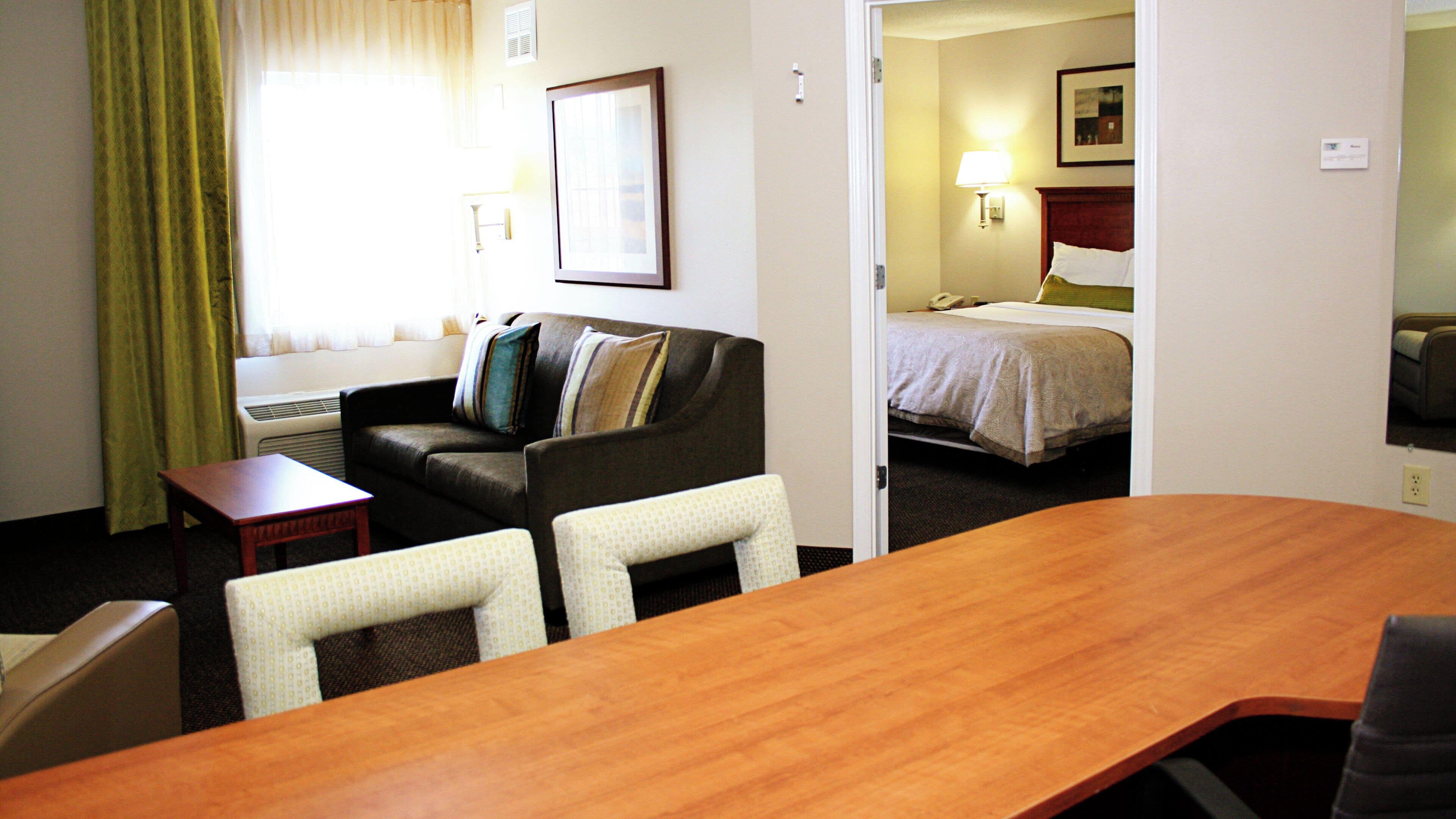 A hotel room with a wooden conference table, a sofa, a bed, and a separate seating area with a chair.