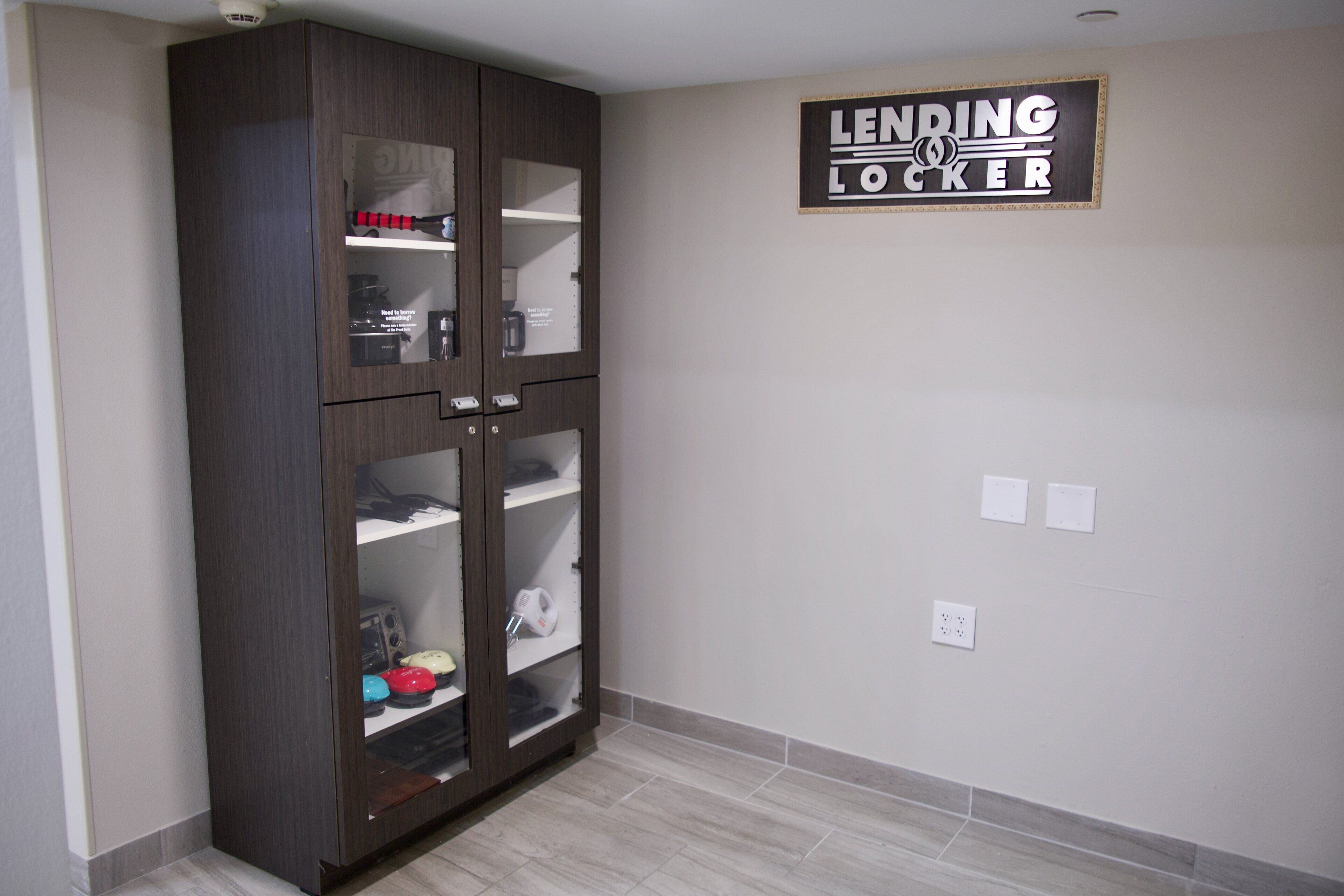 Una habitación con un armario de madera oscura, un letrero en la pared que dice "LENDING LOCKER" y un suelo de baldosas.