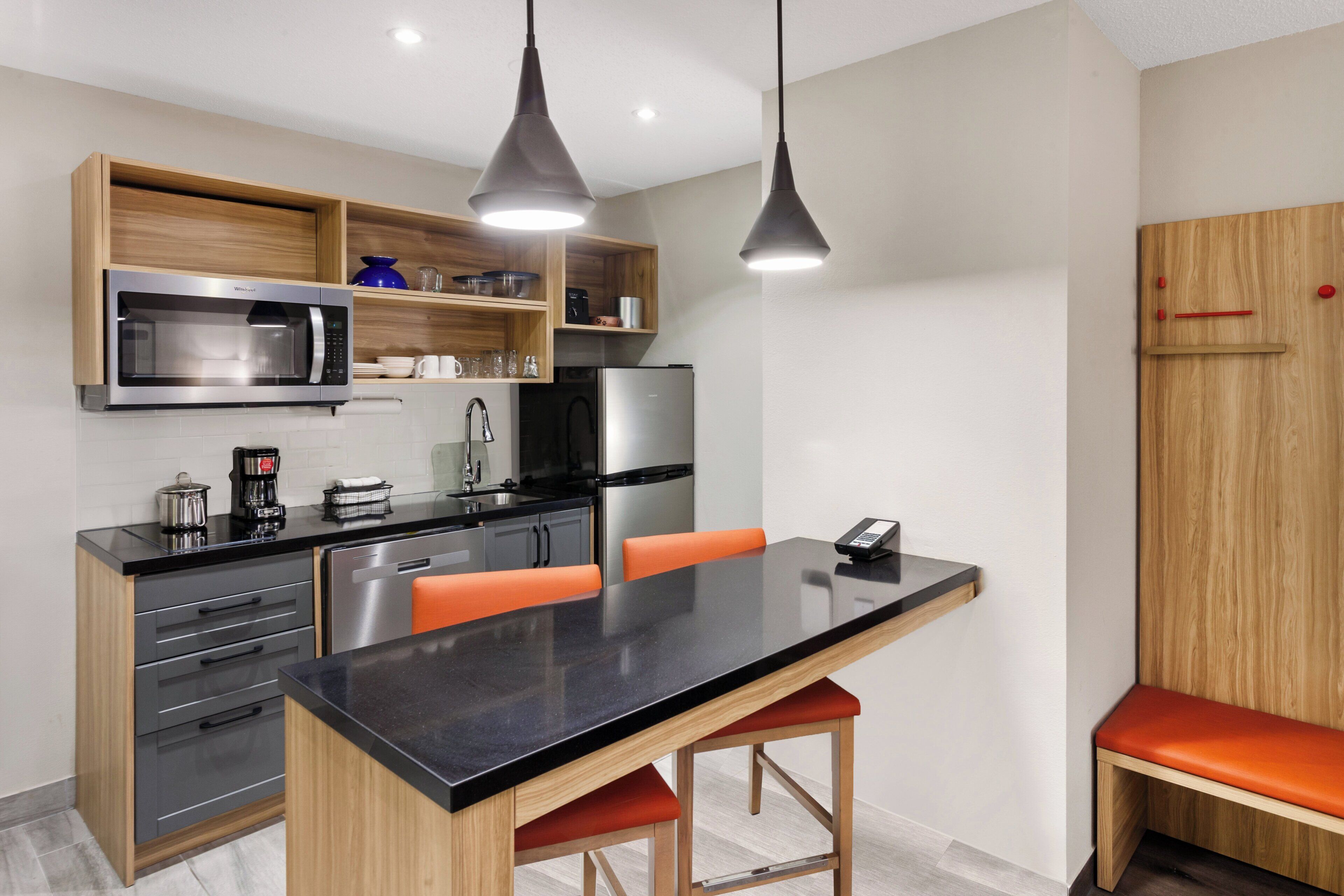 A modern kitchen with a central island, wooden cabinets, stainless steel appliances, and orange chairs.