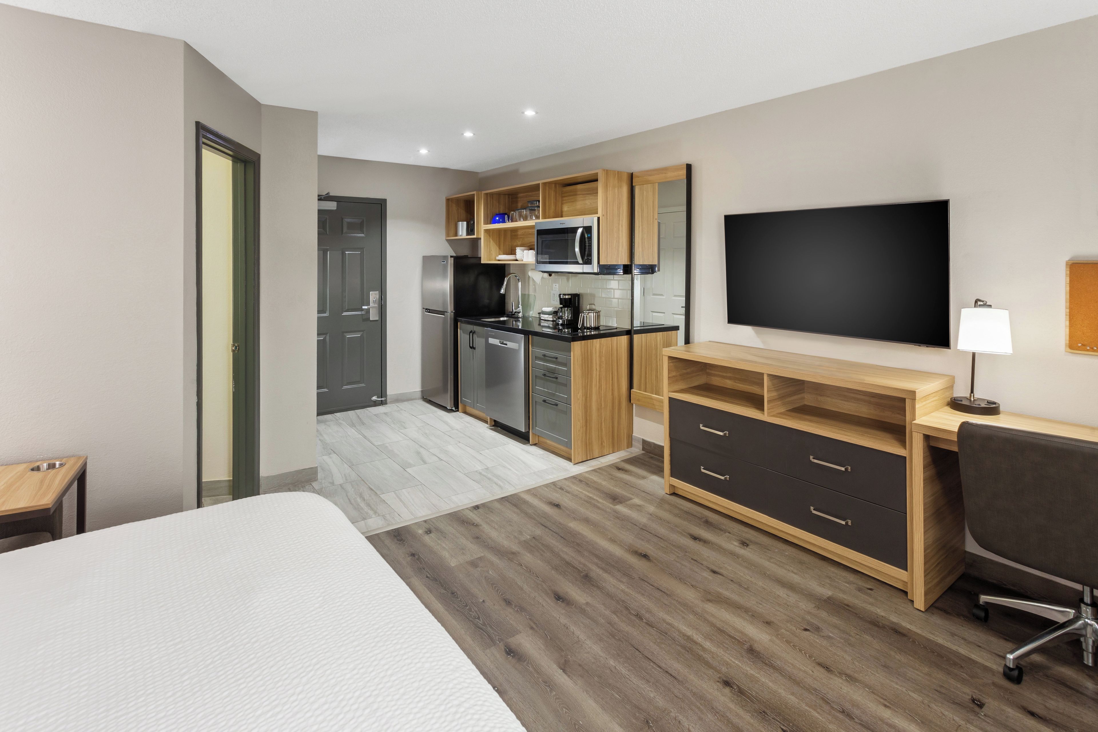 Une chambre d’hôtel moderne dotée d’un grand lit, d’un bureau avec une chaise, d’une télévision à écran plat, d’une kitchenette et d’une salle de bain.