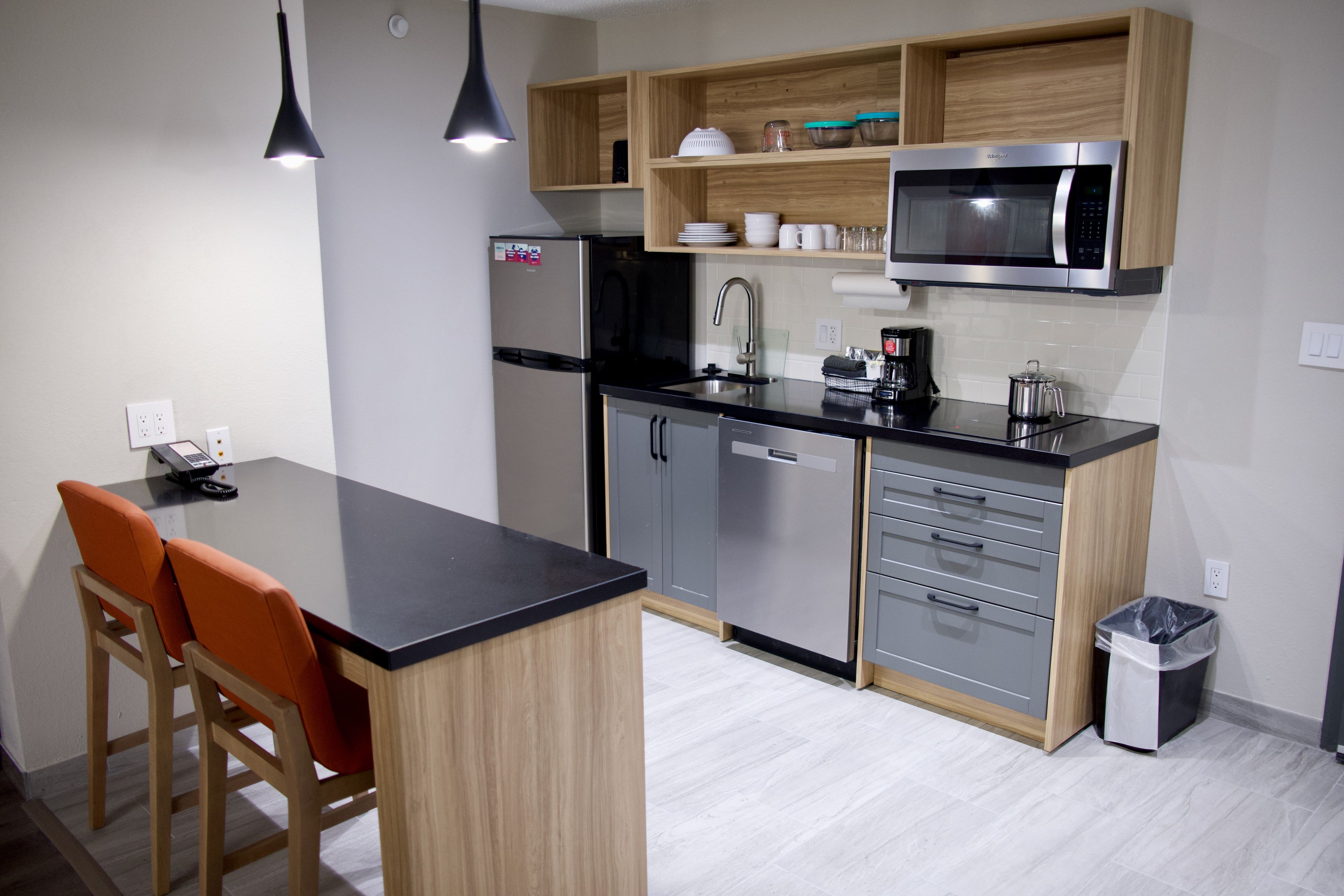 A modern kitchen with a black countertop, wooden cabinets, a stainless steel refrigerator, and a microwave.
