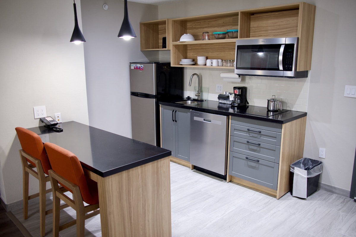 Una cocina moderna con encimera negra, armarios de madera, refrigerador de acero inoxidable y microondas.