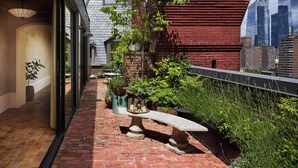 A rooftop garden with a brick pathway, potted plants, and a stone bench. - The Hotel Chelsea (New York)