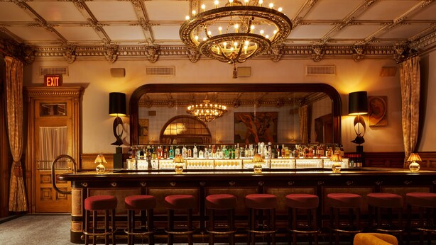 A bar area with a long counter, multiple stools, and a chandelier. - The Hotel Chelsea (New York)