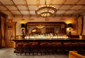A bar area with a long counter, multiple stools, and a chandelier. - The Hotel Chelsea (New York)