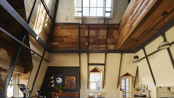 A spacious loft with exposed wooden beams, a large window, and exercise equipment.