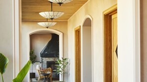 A hallway with a tiled floor, wooden ceiling, and a fireplace. There are two chairs and a table in the background.