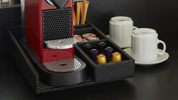 A red espresso machine with a tray of coffee pods and two white cups on a black tray.