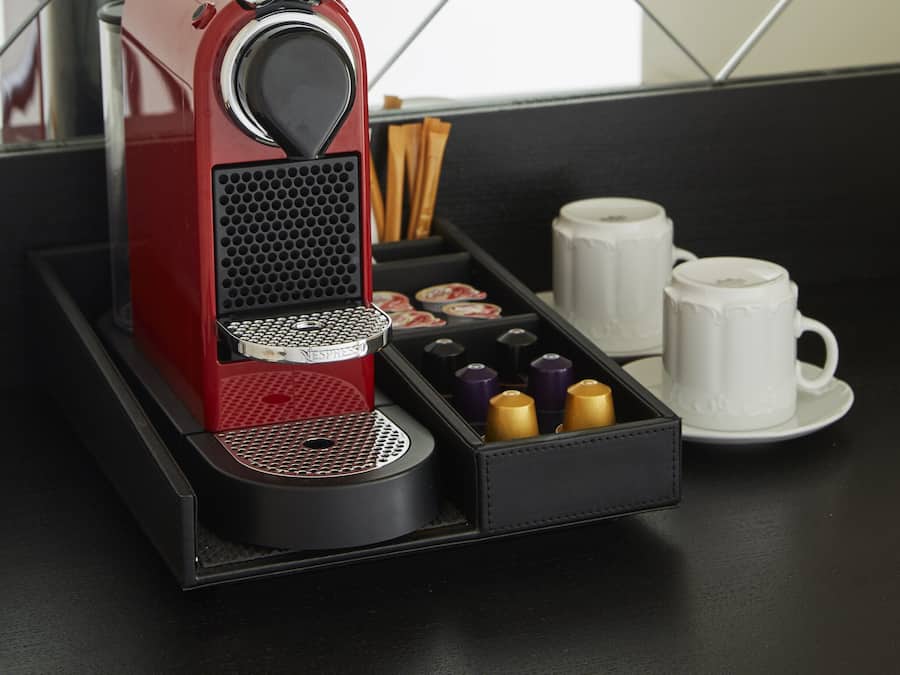 A red espresso machine with a tray of coffee pods and two white cups on a black tray.