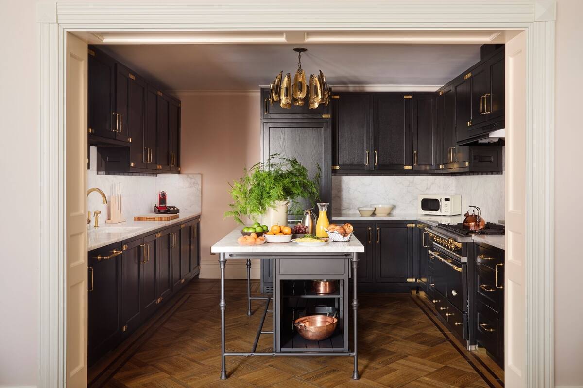 A compact kitchen with dark cabinetry, a central island with a potted plant, and a copper pot on the lower shelf.