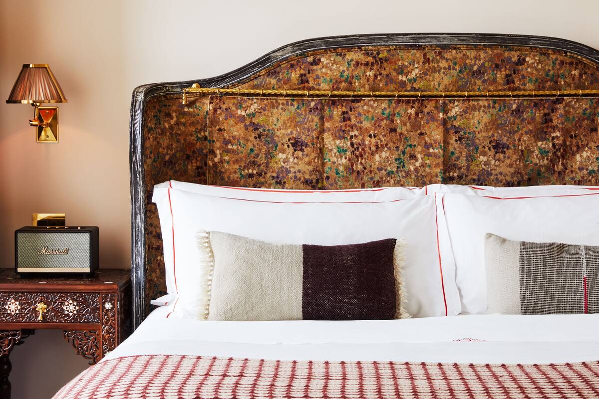 A neatly made bed with white linens and decorative pillows, a vintage radio on a wooden nightstand, and a patterned headboard.